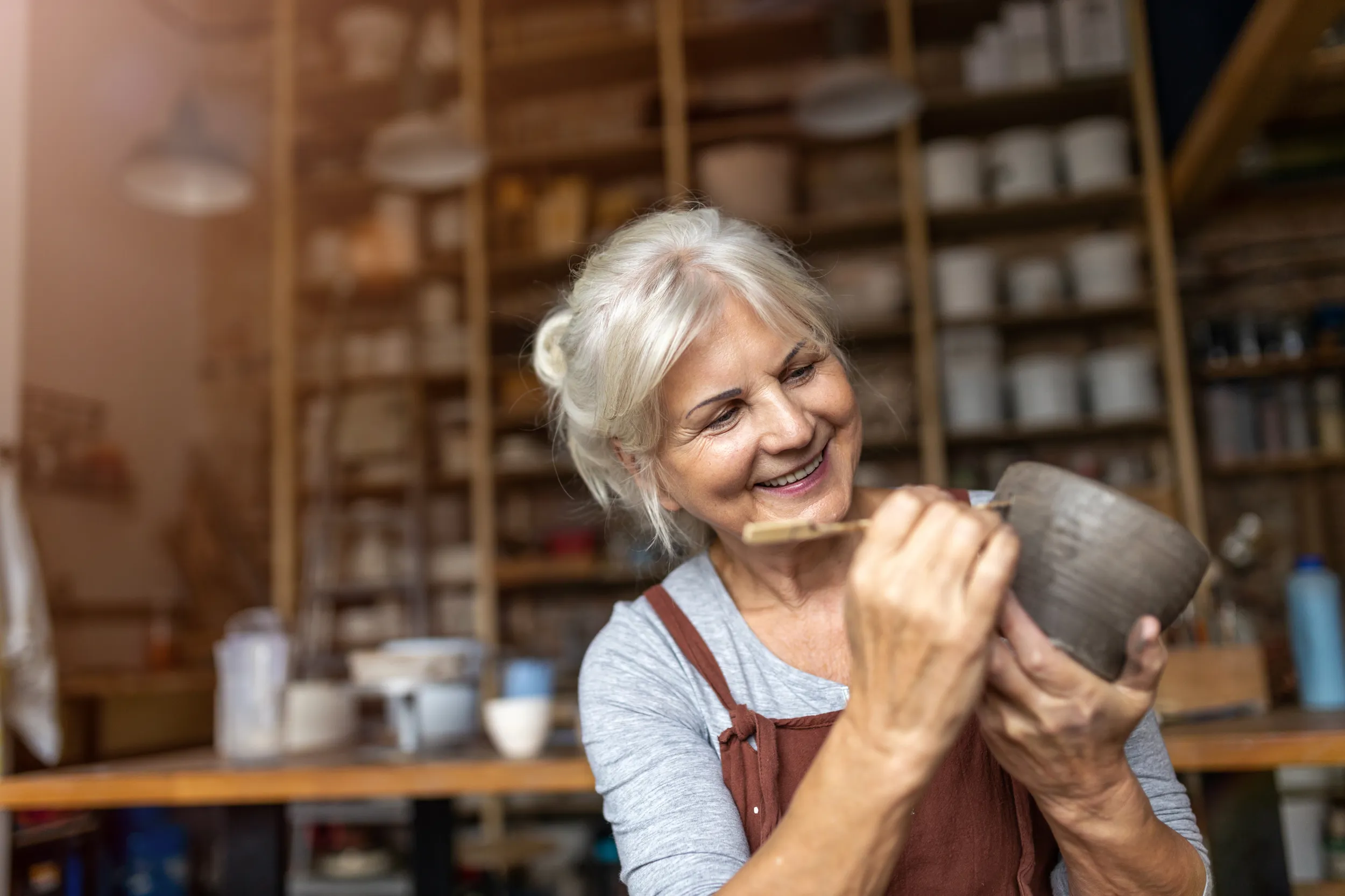 Une femme aux cheveux gris en train de faire de la poterie et du modelage